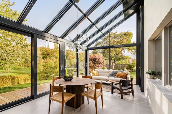 Die großflächigen Glaselemente und das Glasdach mit seinen filigranen Aluminiumsparren öffnen den Blick in den herbstlich gefärbten Garten. 