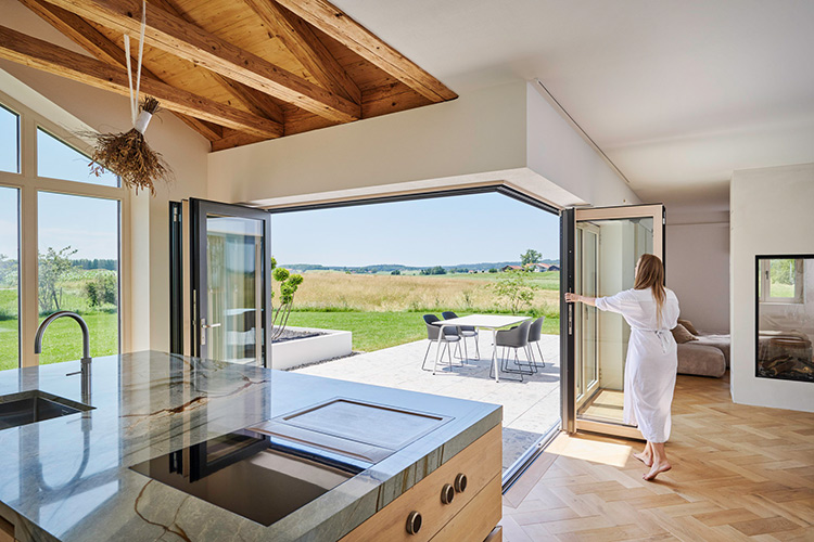 Mit einer Glas-Faltwand lässt sich die Küchen- und Wohnzone mit wenigen Handgriffen zur Terrasse hin öffnen – der Blick in die Landschaft bleibt das ganze Jahr über erhalten.